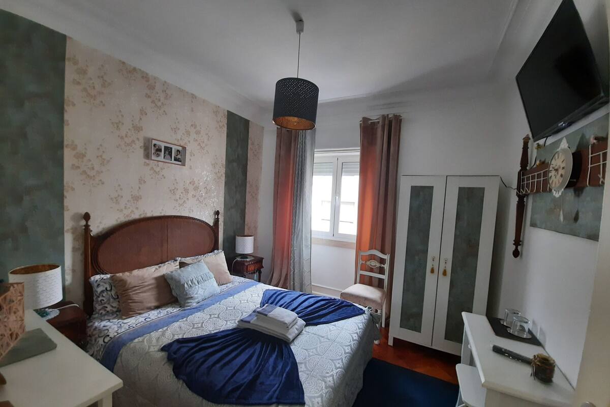 A bedroom with a bed, a bedside table, a lamp, a wardrobe, a TV, and a window with curtains.