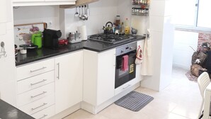 A modern kitchen with white cabinets, a black countertop, and a built-in oven. There is a window providing natural light and a view of the outside. - Ameli Rooms (Lisbon)