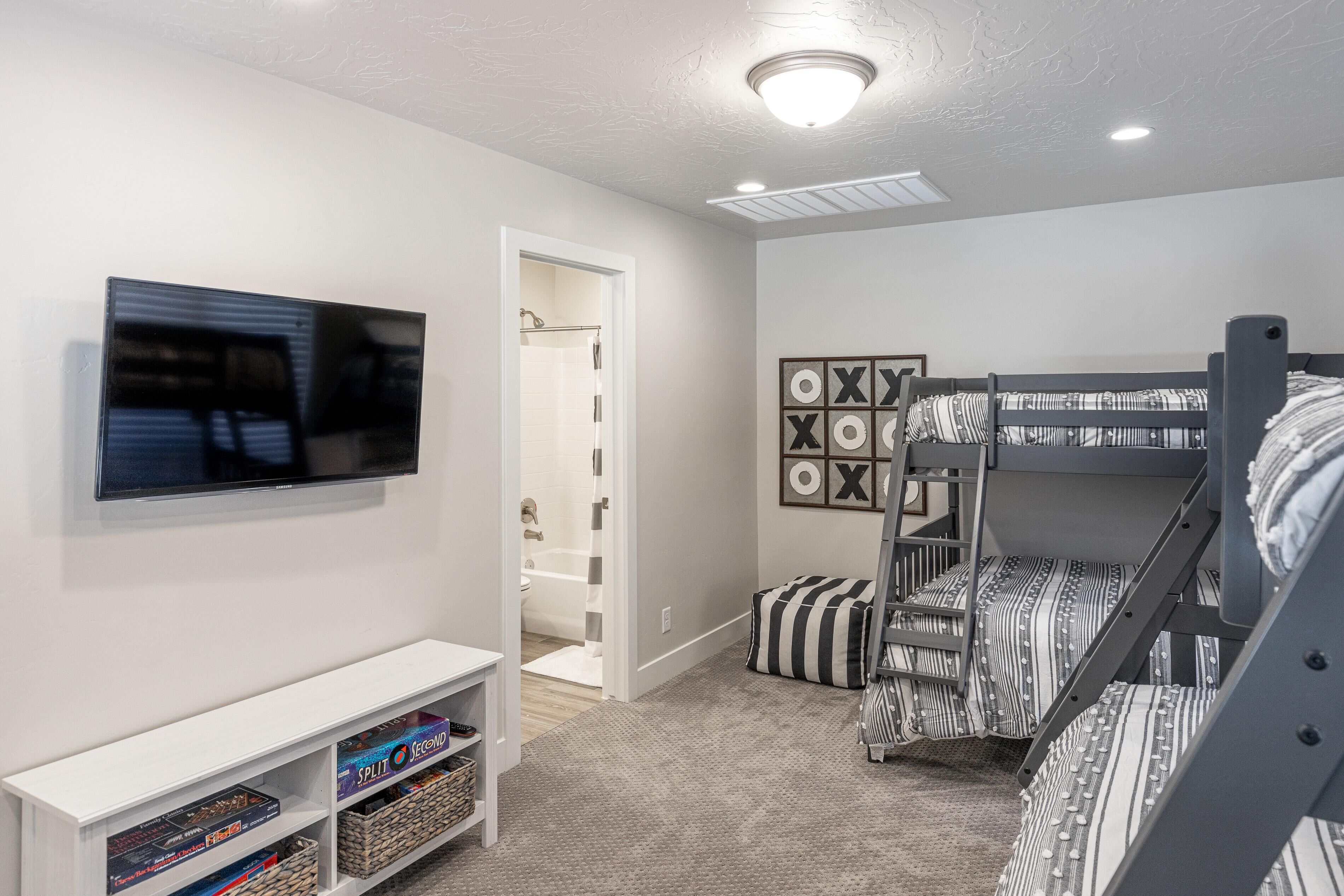 A bedroom with bunk beds, a TV, a bookshelf, and a bathroom visible through an open door.