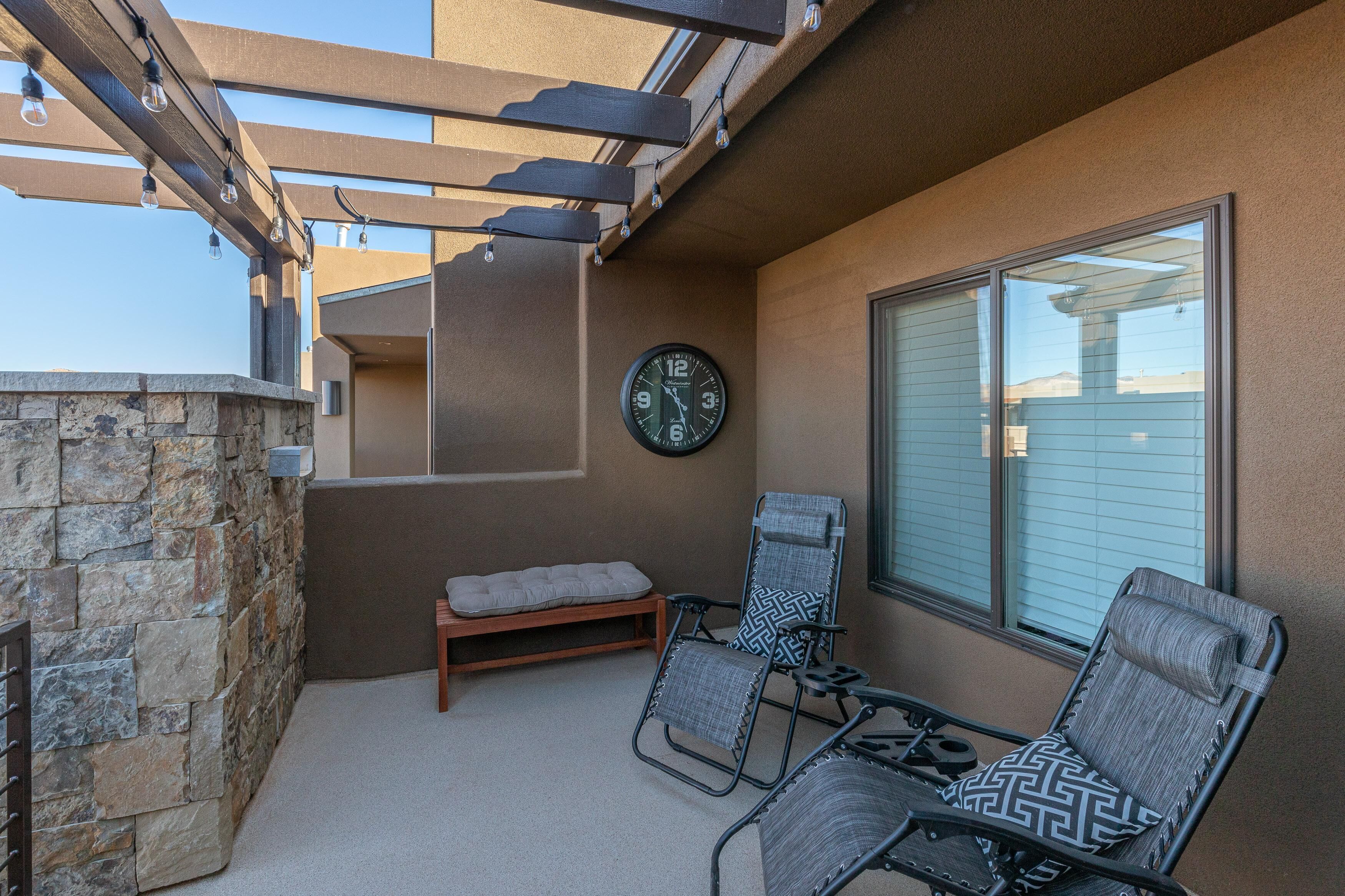 A patio with two chairs, a bench, and a wall-mounted clock.