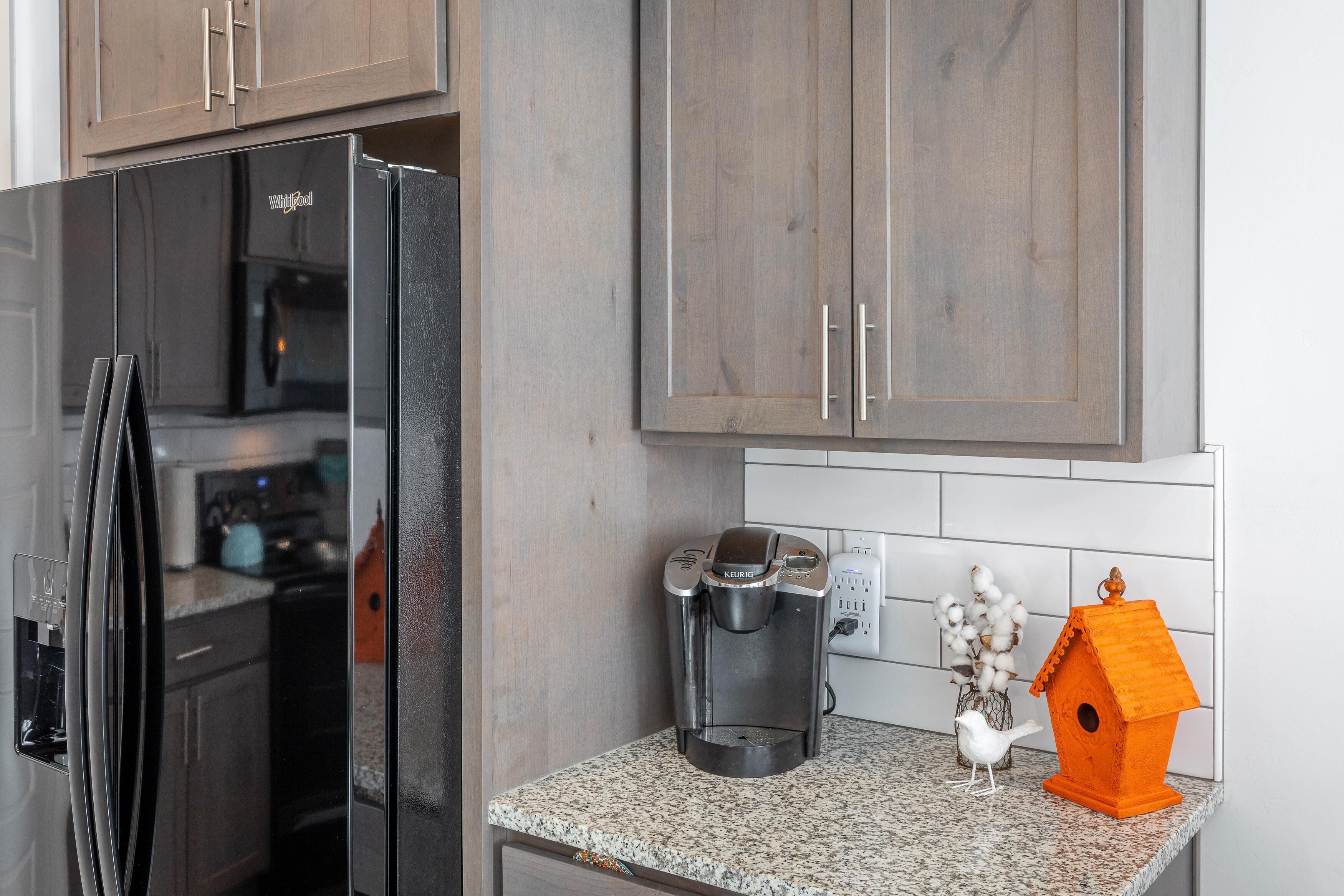 A kitchen with a black refrigerator, a coffee maker, and a birdhouse on the counter.
