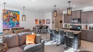 A modern kitchen with bar stools, a dining area with a sofa, and a large abstract painting on the wall.