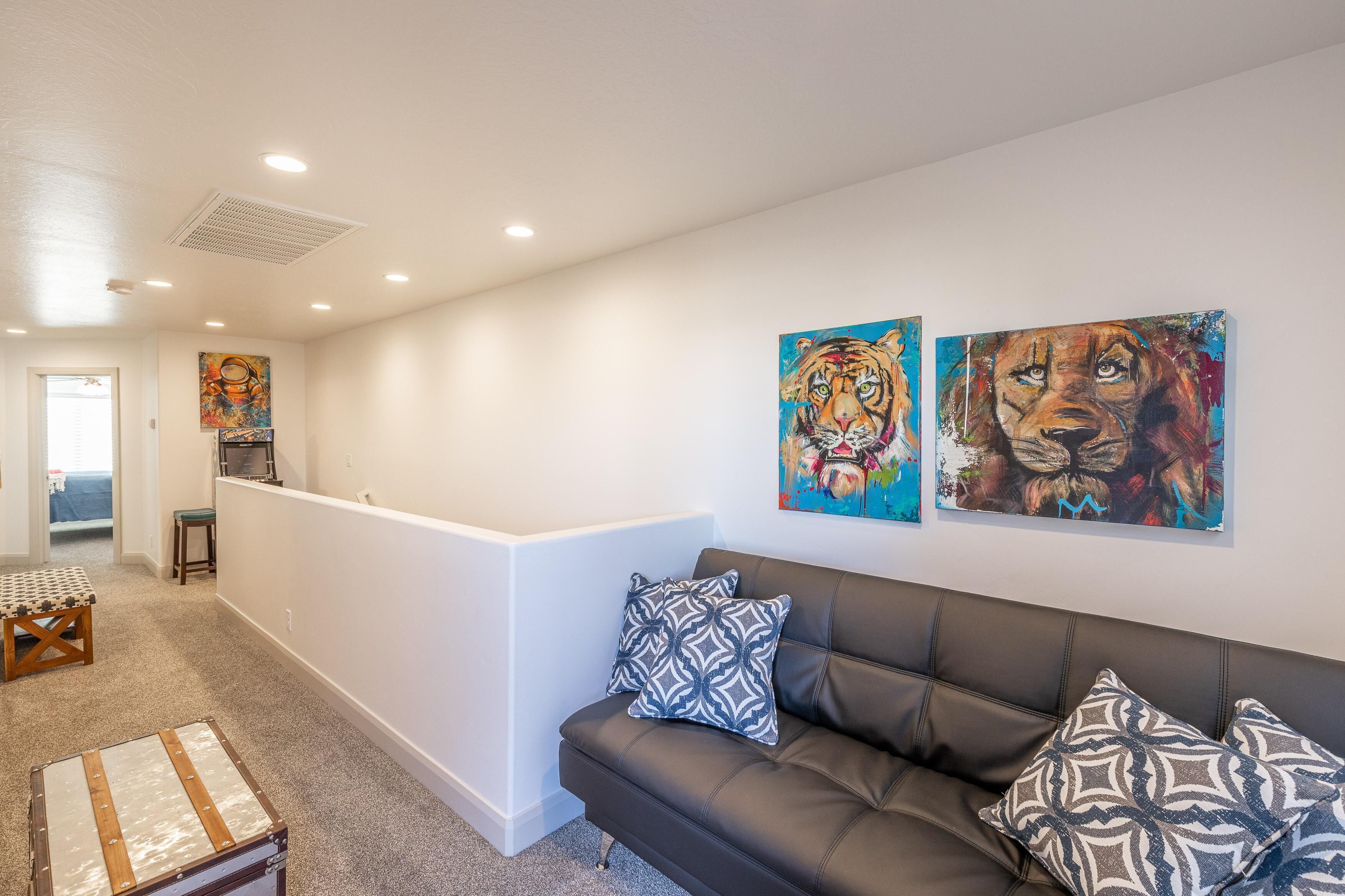 Ein modernes Wohnzimmer mit einem Ledersofa, gemusterten Kissen und zwei großen Tiergemälden an der Wand.