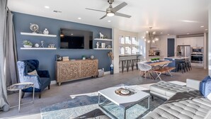 A modern living room with a TV, seating, and a dining area. - Oasis by the Pool (St. George)