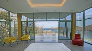 A modern room with large windows, a bed, and two chairs. - Oceanview Escape in Peninsula Papagayo – Pool, Concierge & Resort Access (Peninsula Papagayo)