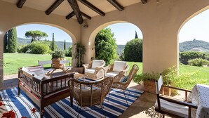 A covered outdoor seating area with wicker furniture, a striped rug, and views of a green landscape.