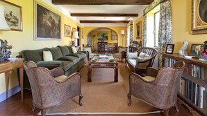 A cozy living room with a green sofa, wicker chairs, a coffee table, and a bookshelf filled with books.