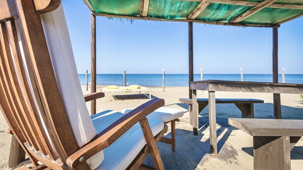 A beachside seating area with wooden chairs and a table, overlooking the ocean.