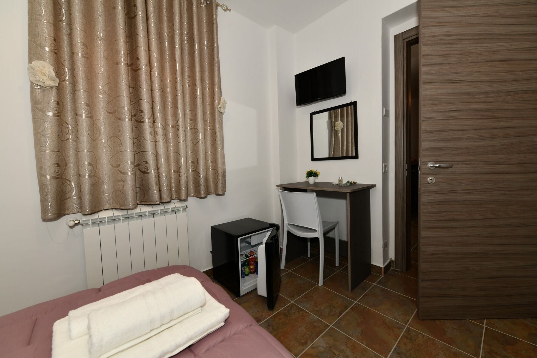 Ein Schlafzimmer mit einem Bett, einem Schreibtisch mit Stuhl, einem Fernseher und einer Tür.