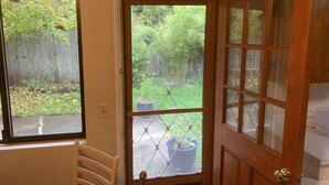 A room with a wooden door, a window, and a view of a backyard with a wooden fence and greenery. - South Hills Rose house (Eugene)