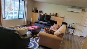 A living room with a sofa, a coffee table, a TV, and a fireplace. - South Hills Rose house (Eugene)