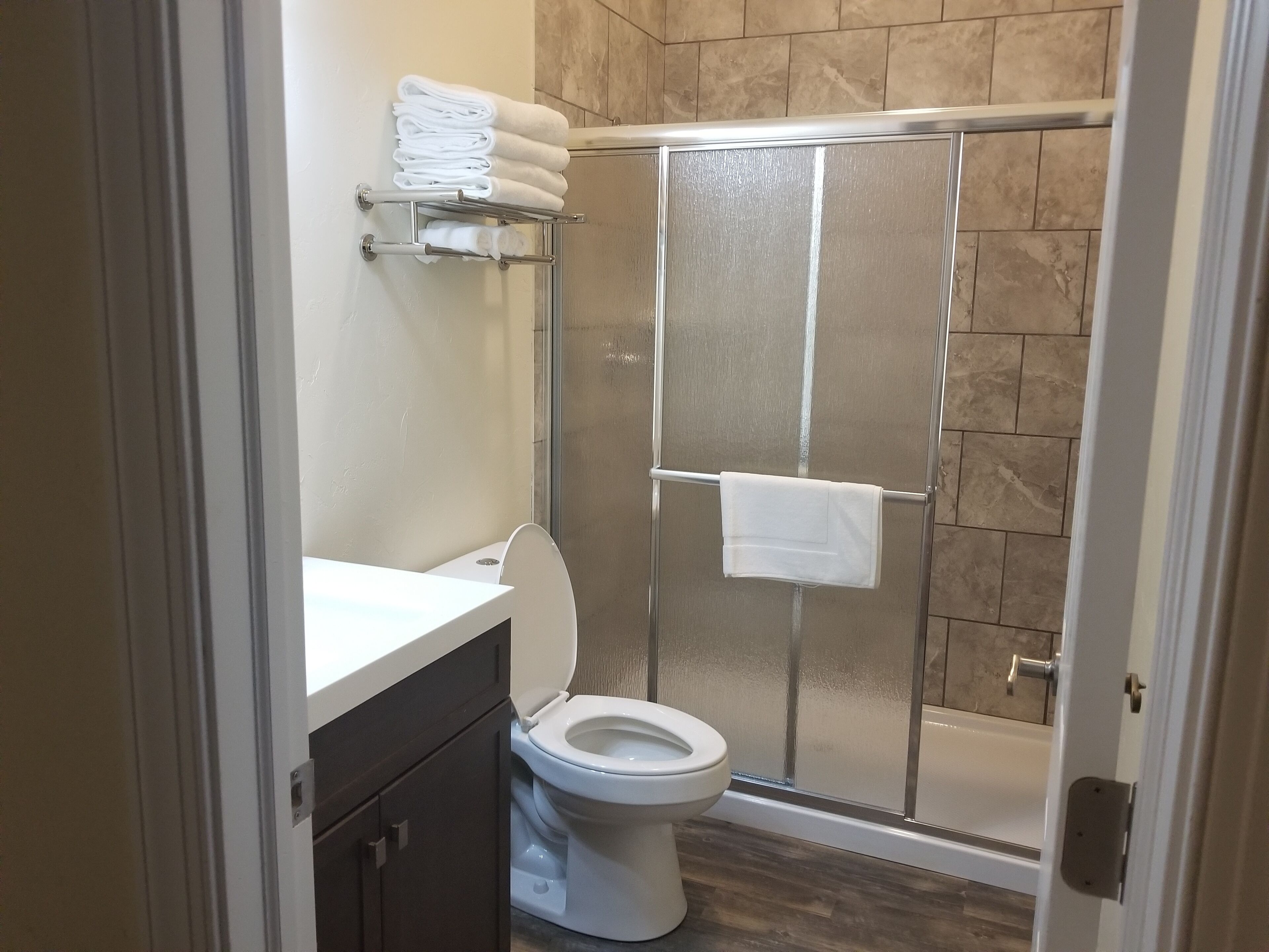 Un bagno moderno con cabina doccia in vetro, vaso bianco e porta asciugamani con asciugamani piegati.