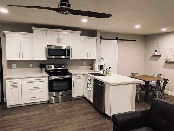 Una cocina moderna con armarios blancos, electrodomésticos de acero inoxidable y una zona de comedor con mesa y sillas de madera.