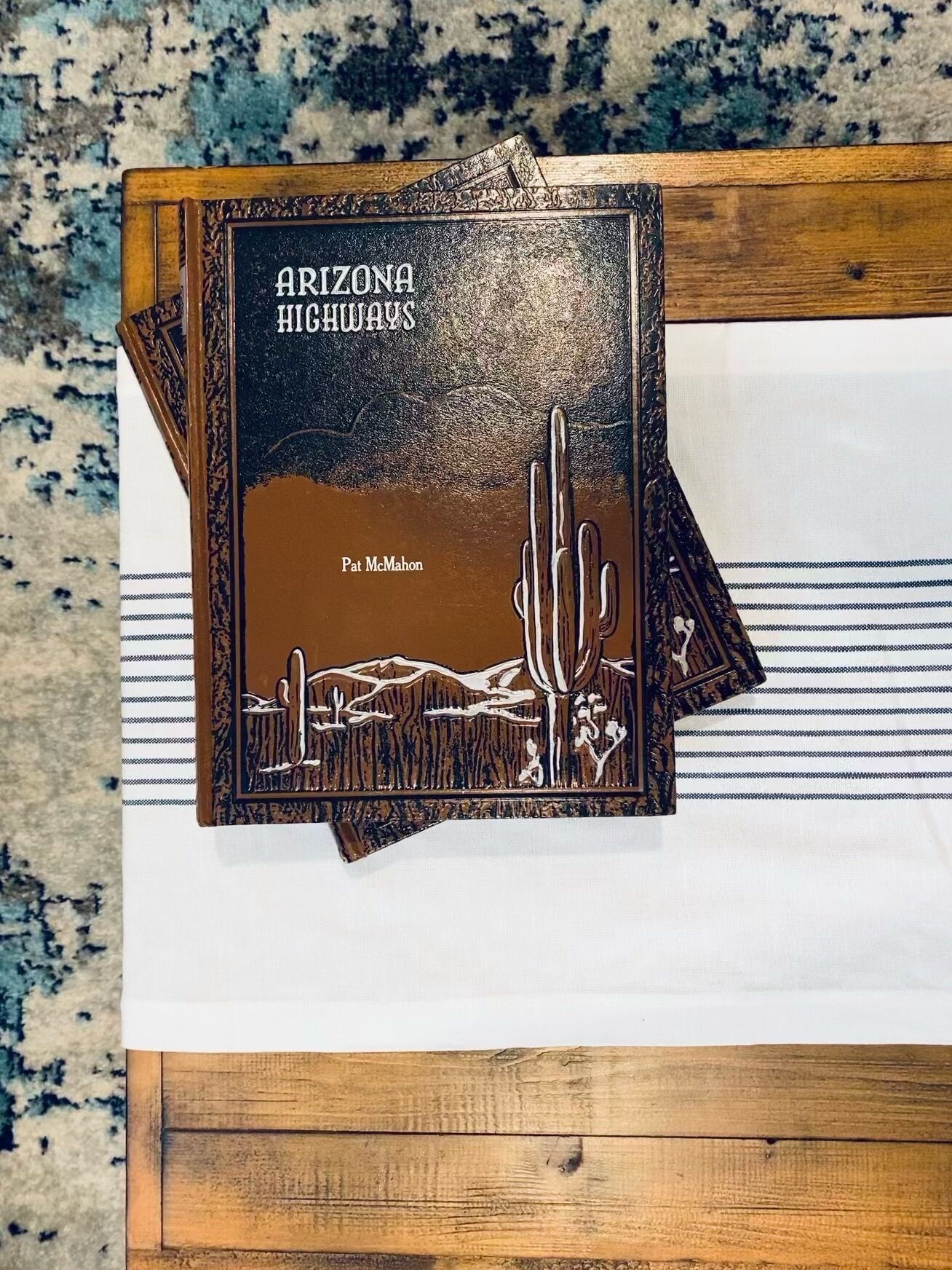 A book titled "Arizona Highways" by Pat McMahon, placed on a wooden surface with a striped fabric underneath.