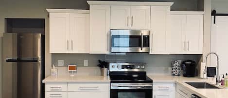 Una cocina moderna con armarios blancos, electrodomésticos de acero inoxidable, un ventilador de techo negro y suelo de madera.