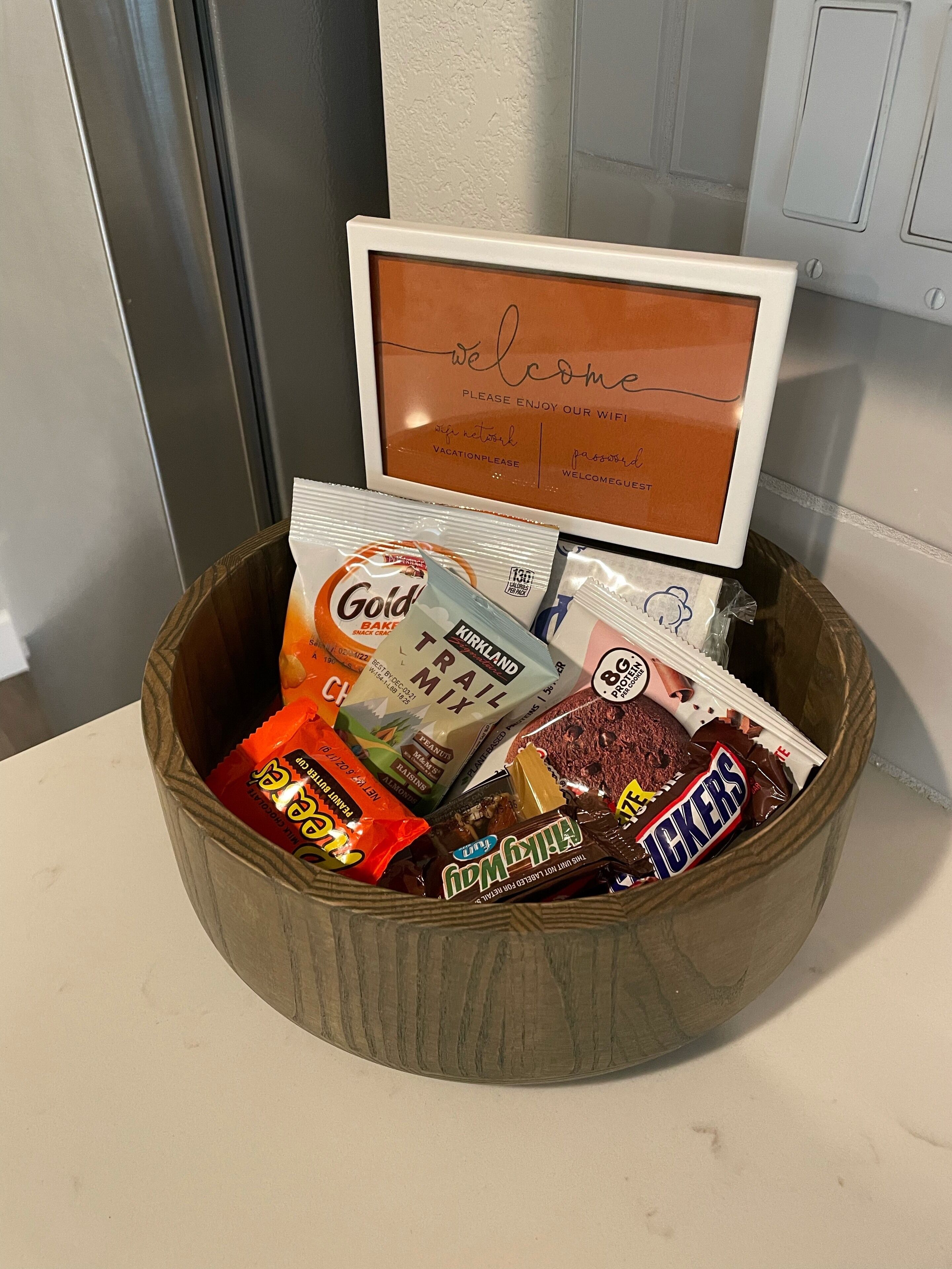 A wooden basket filled with assorted snacks and a framed welcome sign.