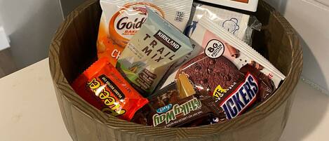 A wooden basket filled with assorted snacks and a framed welcome sign.