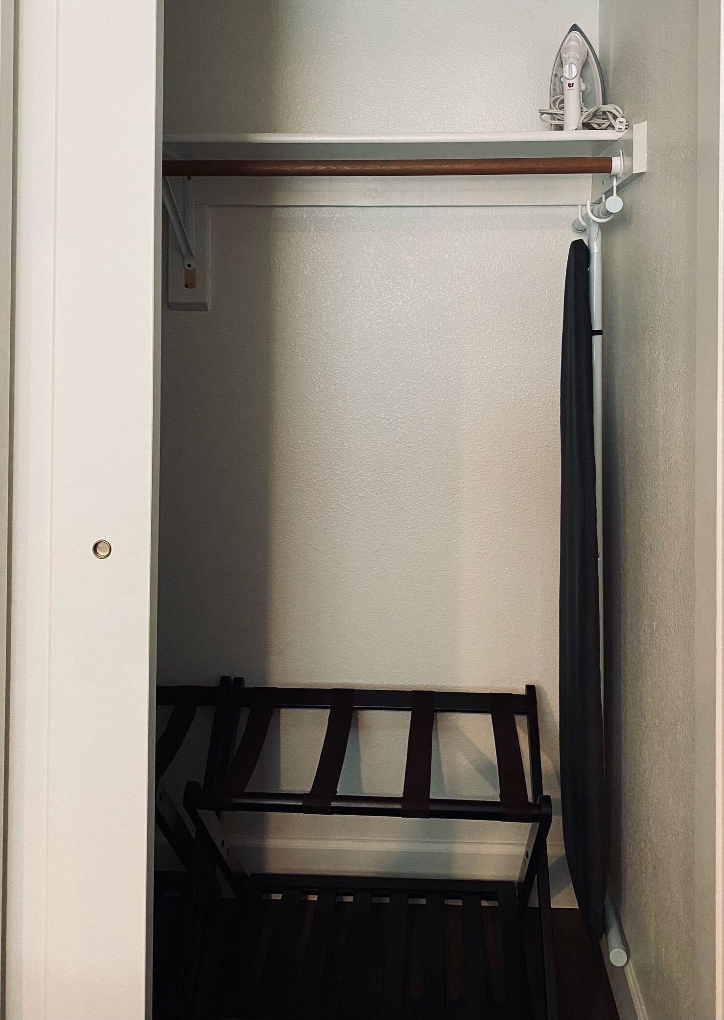A compact room with a bed, a small shelf with an iron, and a door with a lock.