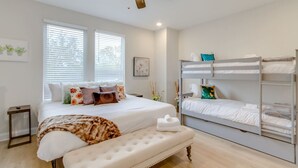 Quarto com uma cama grande, um banquinho e uma cama beliche.