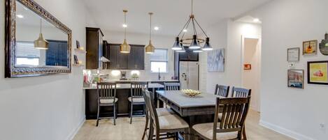 Una cocina moderna con armarios oscuros, una isla central, luces colgantes y una zona de comedor con sillas de madera.