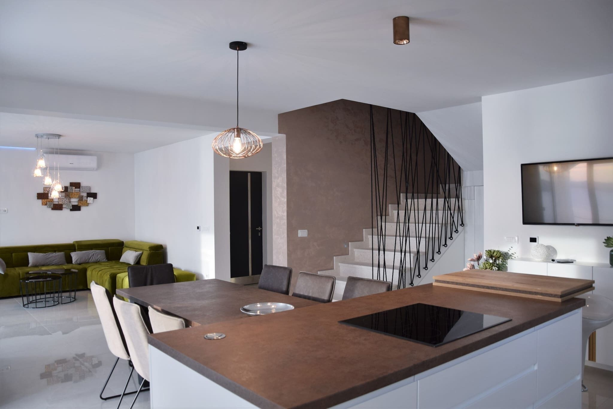 A modern kitchen with a central island, a dining area with a green sofa, and a staircase with a unique design.