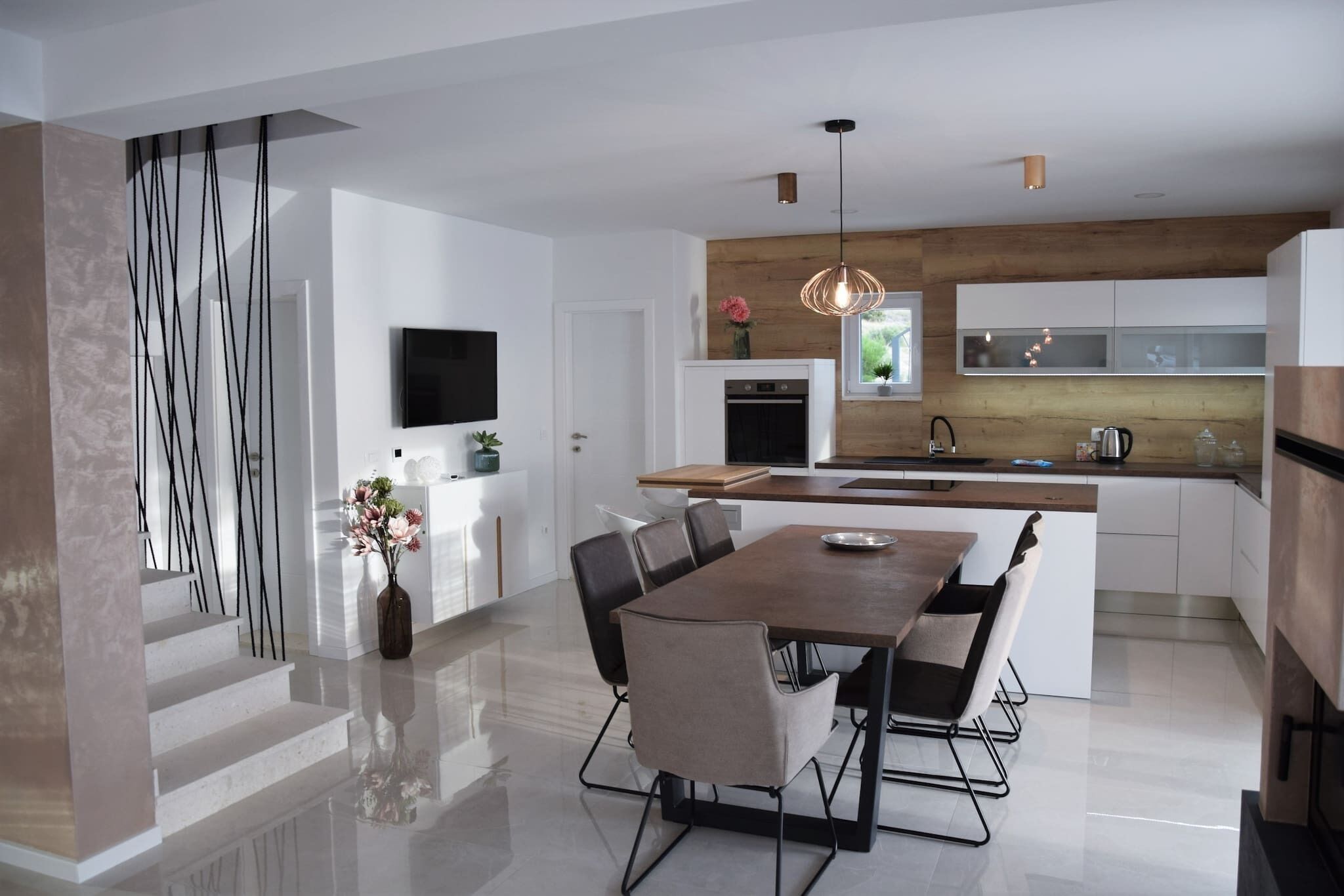 Una cucina moderna con isola centrale, mobili bianchi e una parete decorata in legno.