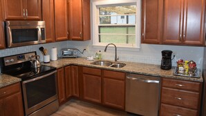 A kitchen with wooden cabinets, stainless steel appliances, a window, and a countertop with various items. - Stay in Franklin - Close to downtown - fire pit & grill (Franklin)