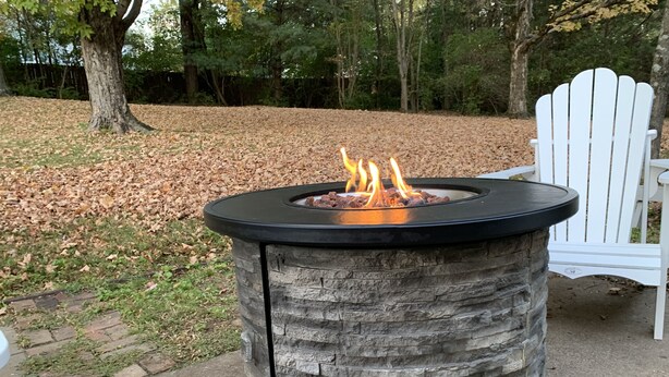 A stone fire pit with a black top, surrounded by a concrete base, set in a park with a white Adirondack chair nearby. - Stay in Franklin - Close to downtown - fire pit & grill (Franklin)