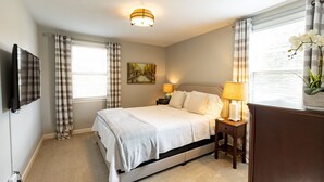 A neatly arranged bedroom with a bed, bedside lamps, a painting, and a television on the wall. - Stay in Franklin - Close to downtown - fire pit & grill (Franklin)