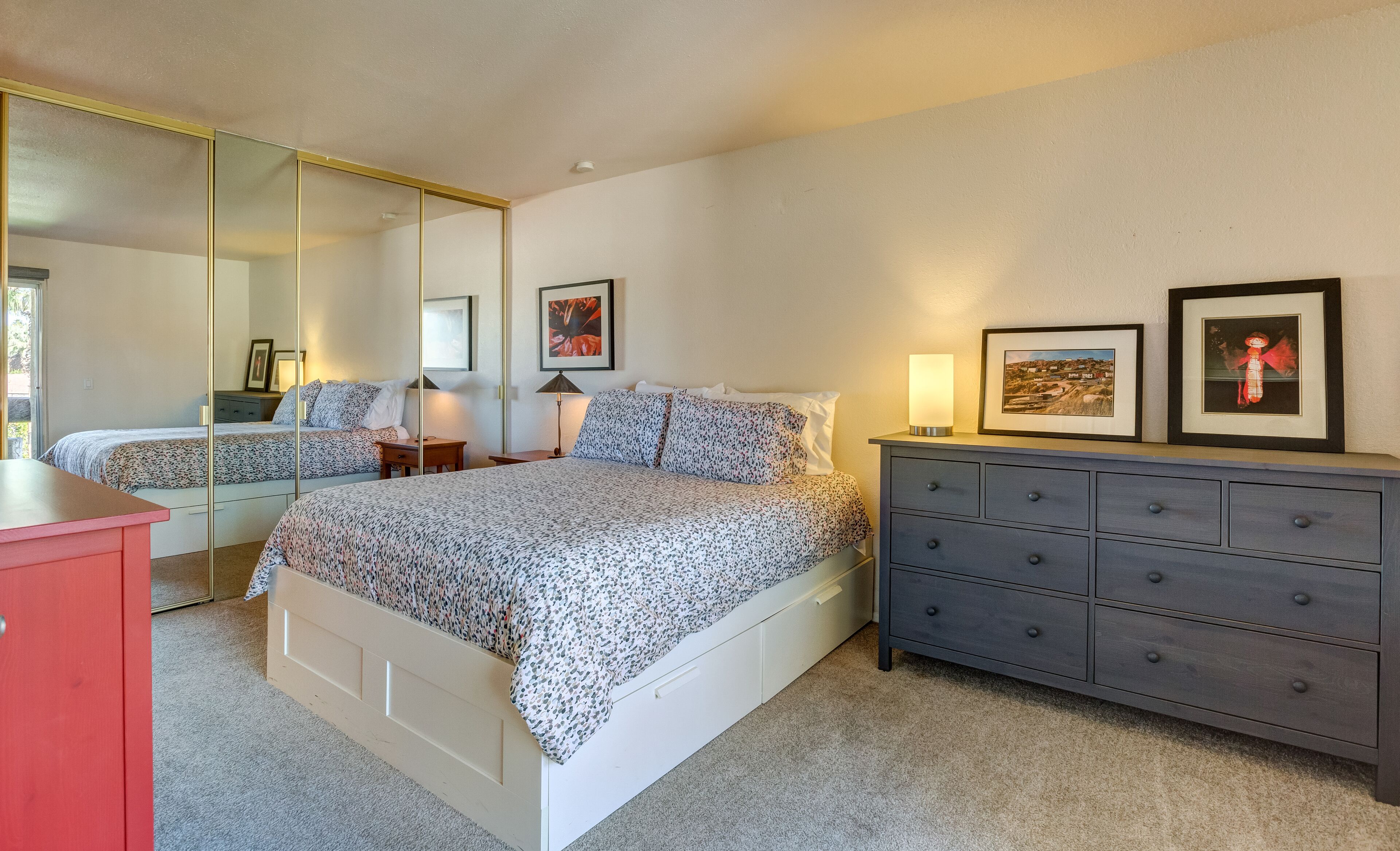 Une chambre à coucher avec un grand lit, une commode, un miroir et des œuvres d’art encadrées accrochées au mur.