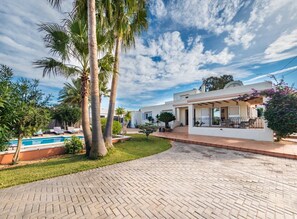Una casa moderna con piscina, rodeada de palmeras y un camino de ladrillos.