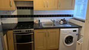 A kitchen with wooden cabinets, a gas stove, a sink, and a front-loading washing machine. - Birmingham city centre apartment  (Birmingham)