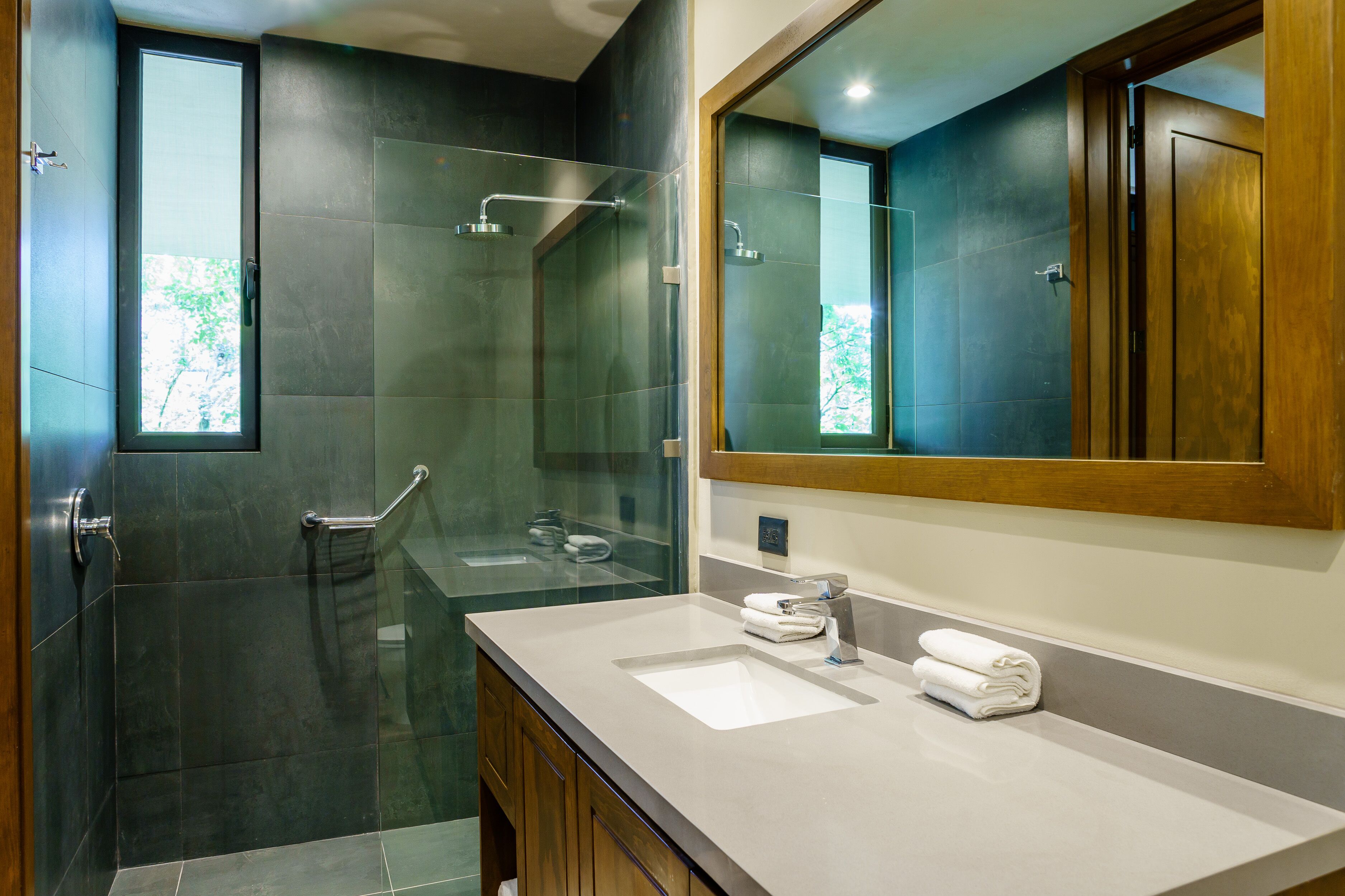 Une salle de bain moderne dotée d’une douche à parois de verre, d’un grand miroir et d’un meuble-lavabo avec deux vasques.