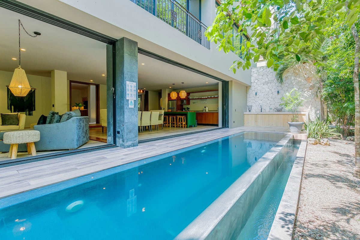 Un espace piscine moderne offrant une vue dégagée sur le salon attenant, qui comprend un coin repas et une cuisine.