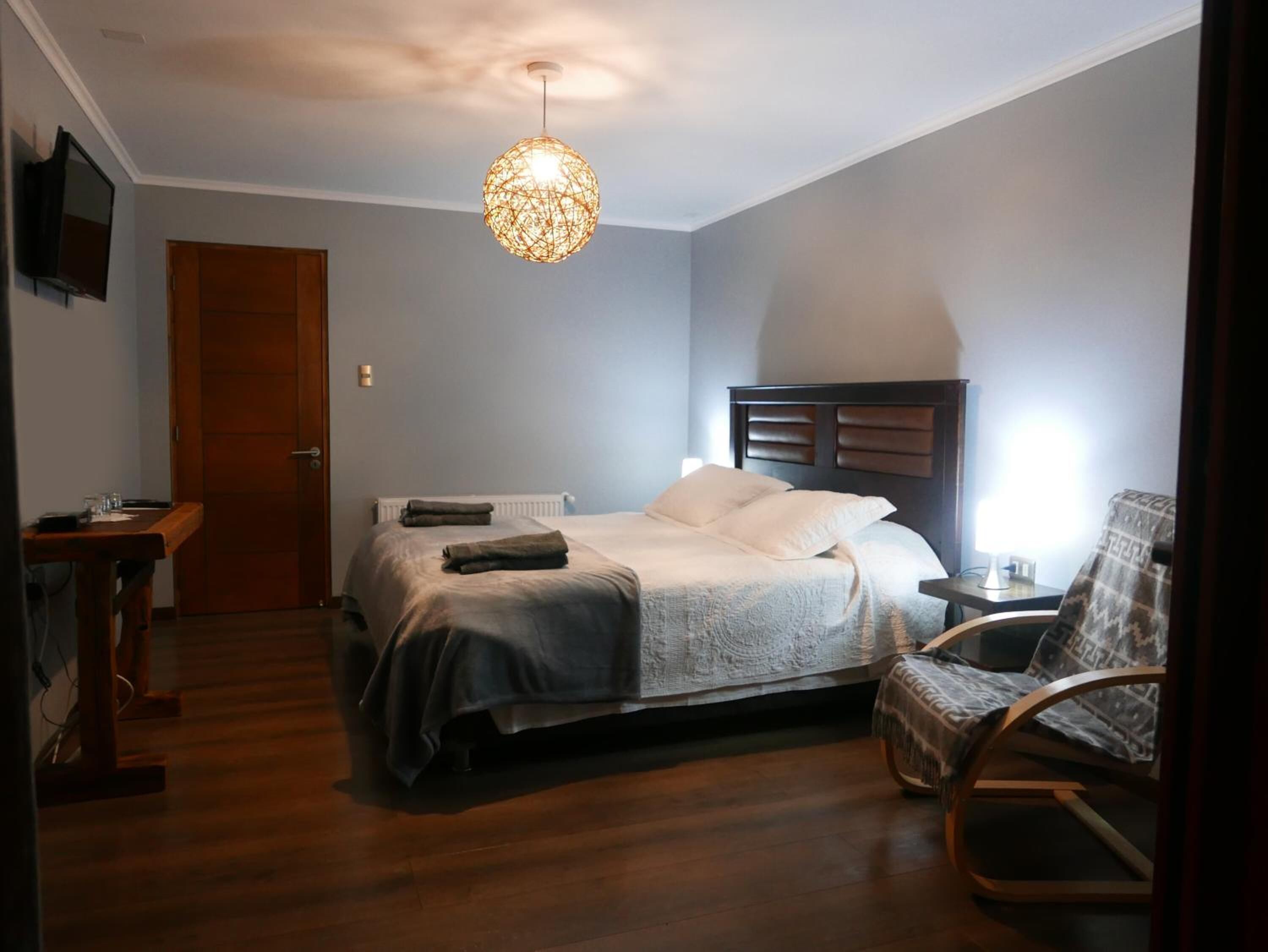 A bedroom with a bed, a chair, a desk, and a television on the wall.