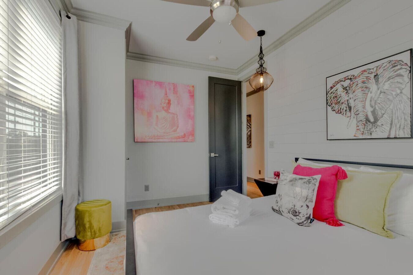 Un dormitorio con cama, ventilador de techo, ventana con persianas y obras de arte en las paredes.