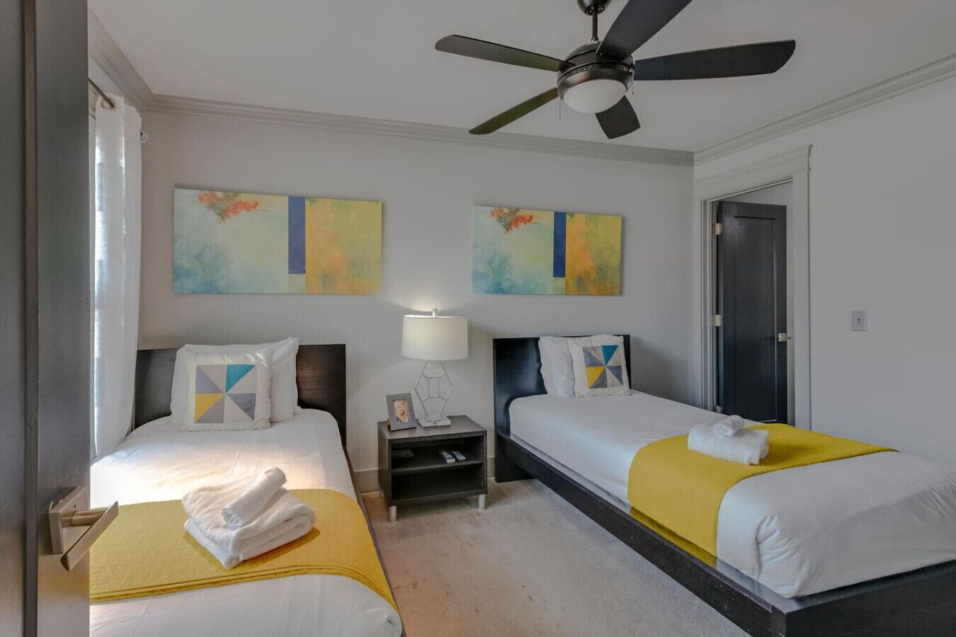 A hotel room with two beds, a ceiling fan, and artwork on the walls.