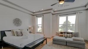 A bedroom with a bed, a sofa, a ceiling fan, and large windows.