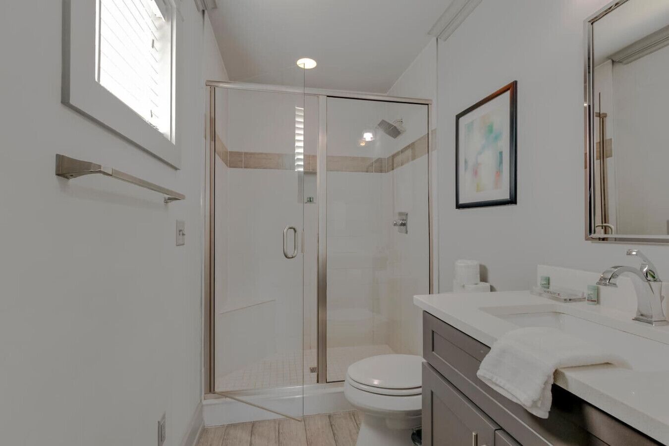Un baño moderno con cabina de ducha de vidrio, inodoro blanco y tocador con espejo.