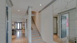 A modern interior with a wooden staircase, a hallway with a glass partition, and a kitchen area in the background.
