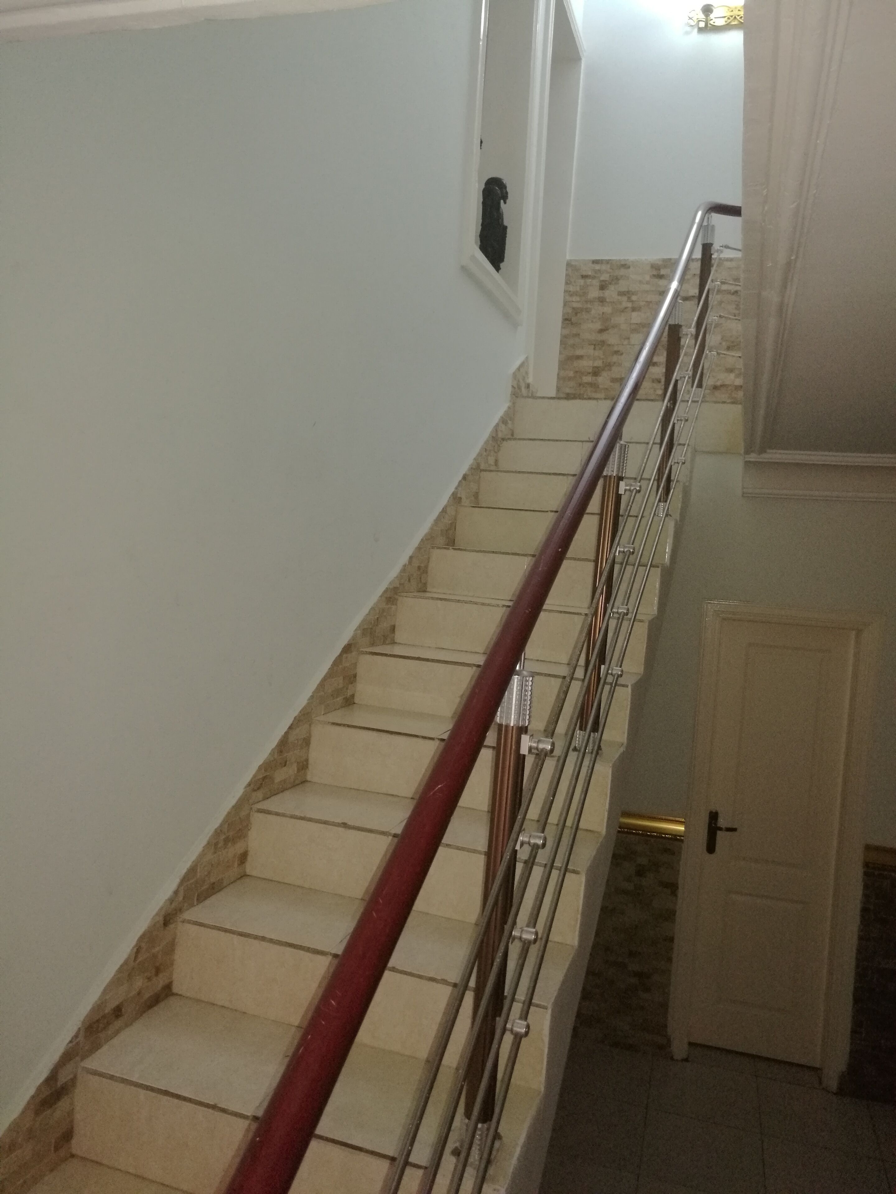 Una escalera con peldaños color beige y barandal rojo, que lleva a una puerta en la parte superior.