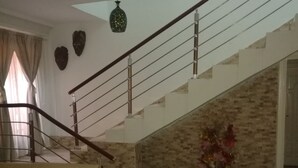 A modern living room with a beige sofa, a staircase with a glass railing, and a decorative plant. - Casa Suit Capir (Malabo)
