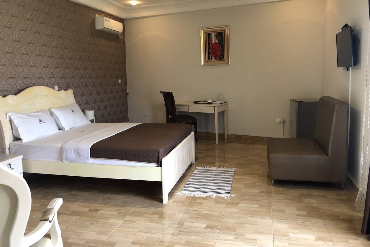 A hotel room with a bed, a desk, a chair, a sofa, and a small table.