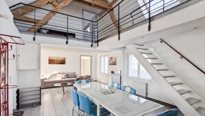 Ein modernes Interieur mit Essbereich, ausgestattet mit einem Glastisch und blauen Stühlen, einer Treppe und einem Wohnzimmer mit Sofa und Kunstwerken.