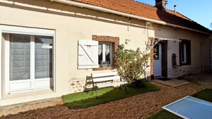 Ein Haus mit Ziegeldach, Schornstein und einem Garten mit Bank und kleinem Baum.