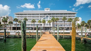 A waterfront hotel with a wooden dock leading to the building, surrounded by palm trees and water. - 2 Side-by-Side Waterfront Condos • 4BR/4BA • Walk to Beach (Clearwater)