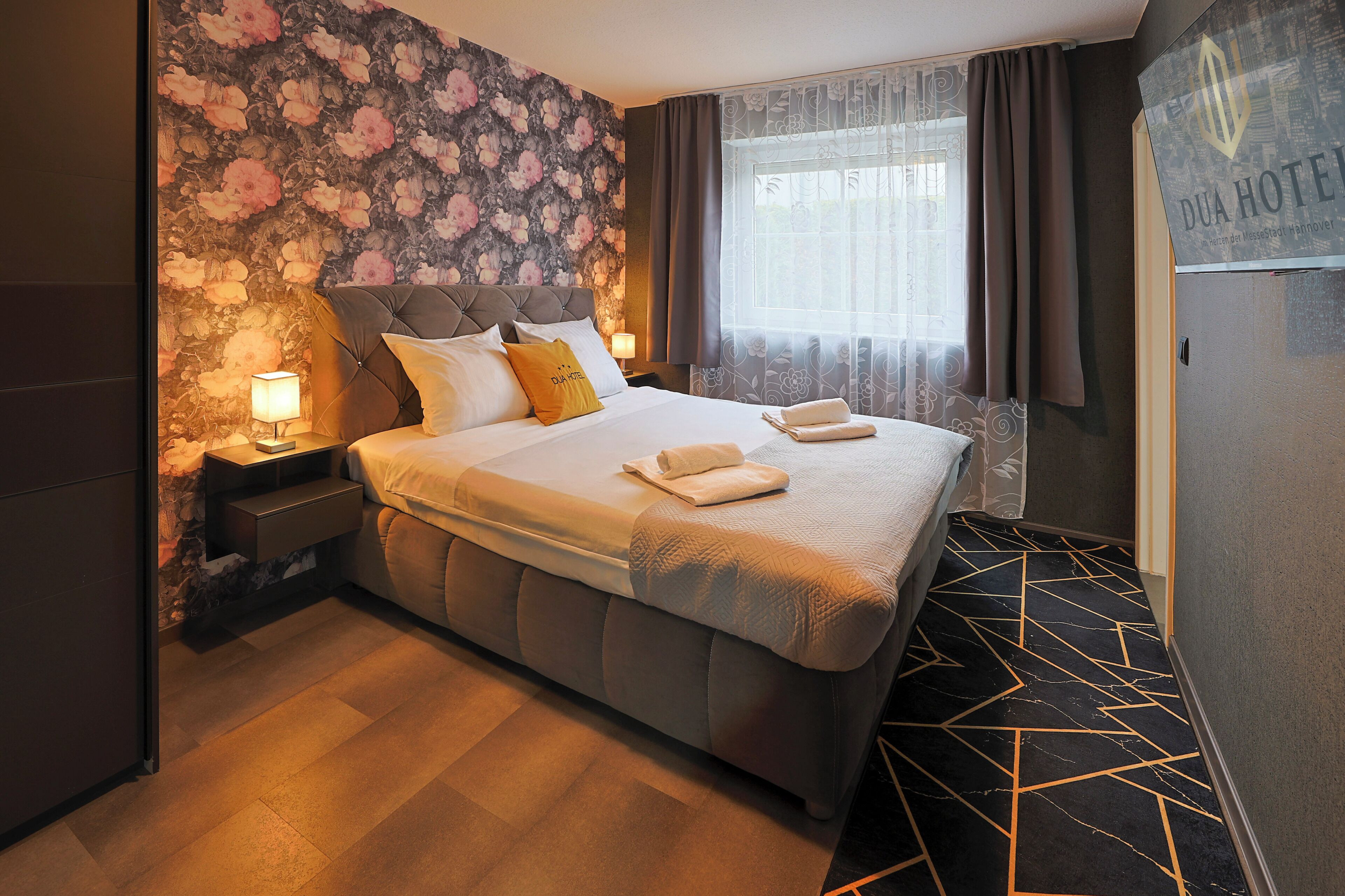 Ein Hotelzimmer mit einem großen Bett, einem Nachttisch, einer Lampe und floralem Wandpapier.