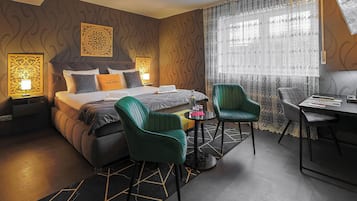 Habitación de hotel con cama, dos sillas, un escritorio y una ventana con cortinas.