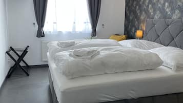 Ein Hotelzimmer mit einem Bett, einem an der Wand befestigten Fernseher, einem Fenster mit Vorhängen und einer Wand mit einem Blattmuster.