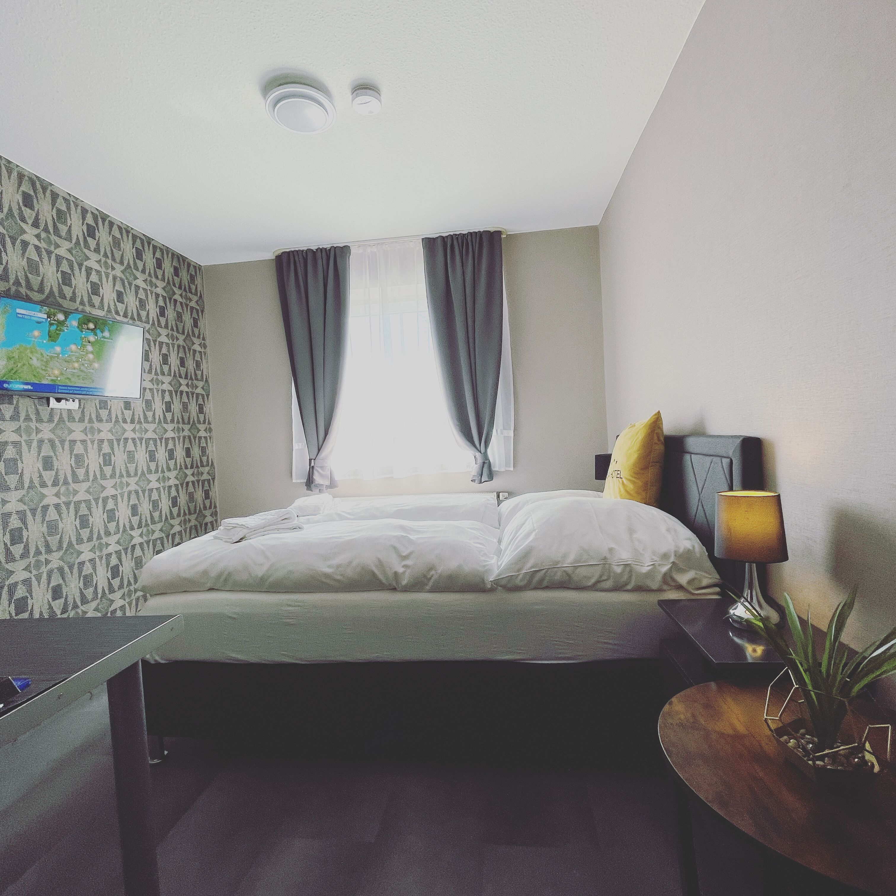 A hotel room with a bed, a desk, a lamp, and a TV on the wall.